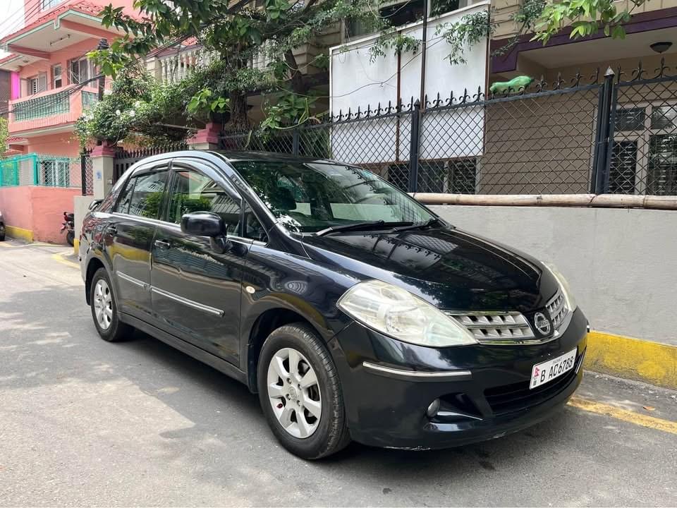 My black 2010 Nissan Tiida sedan, seen from the front left, parked on a Kathmandu street
